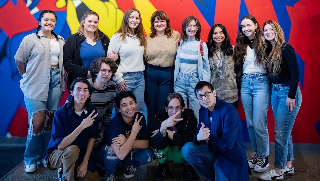 diverse group of students from the U of A in Forth Smith standing in front of a colorful mural